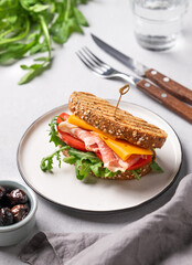 Toast club sandwich made of grain bread with cheddar cheese and bacon stuffed with tomatoes and ruccola on a light background