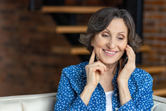 Happy smiling caucasian senior woman calling on mobile phone sitting at home on the couch