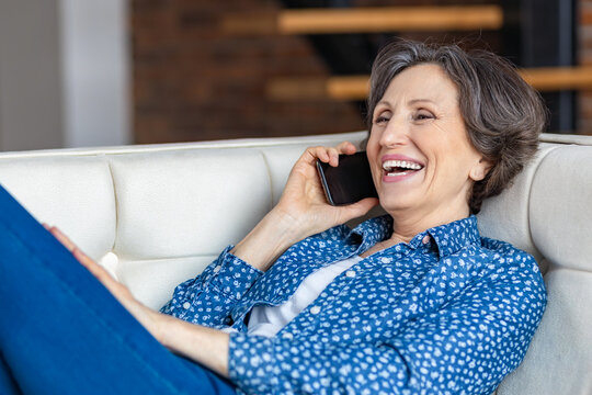 Happy smiling senior woman calling on mobile phone lying on the sofa at home