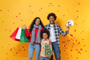 Happy African American family in festive Christmas celebration studio shot yellow color background with confetti - obrazy, fototapety, plakaty
