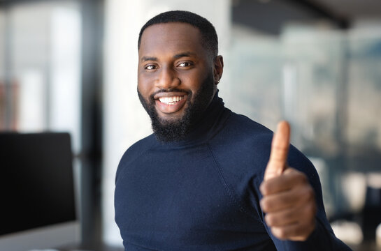 Portrait of successful positive cheerful African American man entrepreneur or office worker in a modern office, looking at the camera and smiling