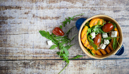 panorama of an pumpkin salad with arugula and feta and tomato on a wooden background