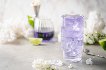 Summer refreshing drink. Light purple cocktail on a white background with spring flowers.