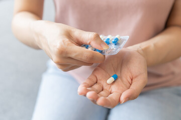 Sick ill asian young woman, girl hand taking tablet pill capsule out from blister pack, painkiller medicine from stomach pain, head ache, pain for treatment, take drug or vitamin at home, health care.