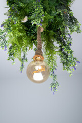 Hanging lamp made with hanging plant leaves and a large round bulb inside which we can see the word love