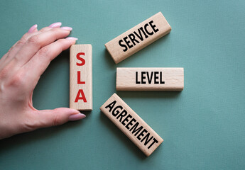 SLA - Service Level Agreement. Wooden blocks with word SLA. Businessman hand. Beautiful grey green...