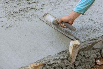 Mason leveling fresh concrete pavement with wet cement using special working tools