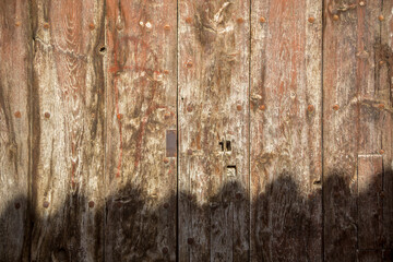 Old and worn vertical wooden slatted door with two leaves and metal lock