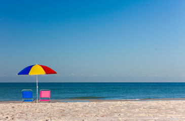 Colorful Umbrella with Pink and Blue Deckchairs on an Empty Beach
