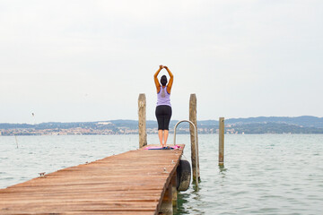 woman makes a yoga pose next to a lake on a pier