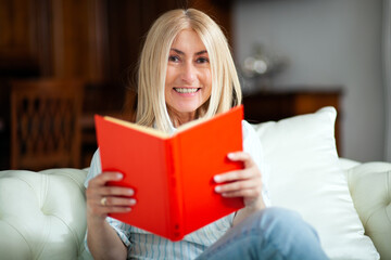 Mature woman reading a book at home on her couch