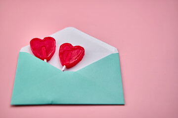 Love letter with two heart-shaped red lollipops inside on a pink background