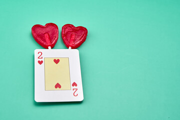 Representation of love between two people with two red heart-shaped lollipops under a two of hearts card on a greenish background.