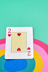 Poker card of the two of hearts on top of a rainbow, with a greenish background. concept of love.