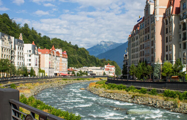 Krasnaya polyana, Krasnodar Krai, Russia - July, 29, 2023: the embankment of the Mzymta River and modern architecture with luxury apartments among green hills on Krasnaya Polyana on a sunny summer day