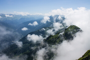 Dramatic landscape - white clouds among the peaks of the mountains against the blue sky on a sunny day and a space to copy