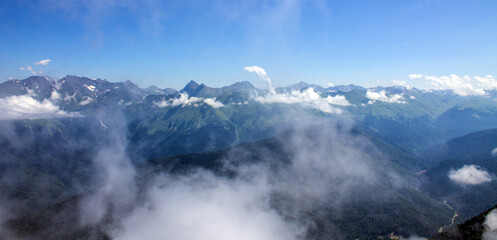 Dramatic landscape - white clouds among the peaks of the mountains against the blue sky on a sunny day and a space to copy