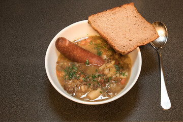 Lentil soup with sausage in a bowl with bread on the side - german stew