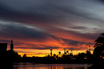 Naklejka premium Dramatic sunset. Yellow, orange and red evening sky. Silhouettes of palm trees and park amusements