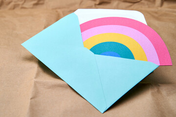 Blue envelope with a rainbow card inside, on a cardboard surface.
