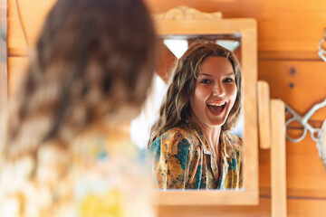 Young woman smiling while looking herself in a mirror at home.