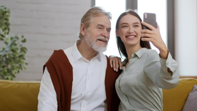 Happy young woman making selfie on smartphone with her senior grandfather, tracking shot, slow motion