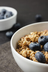 Granola with blueberry in white bowl on dark napkin.