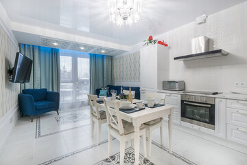 Luxury apartment with a snow-white kitchen set, with an elegant table setting. Bright .blue sofa and armchair in the living room area.