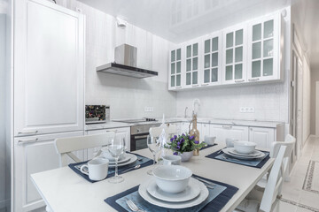 A table with a beautiful setting in the interior of the kitchen with white furniture.