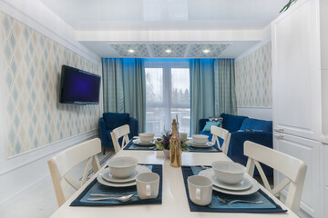 Elegant table setting in the interior of a luxurious living room. A large TV on the wall, .a bright blue sofa and an armchair.