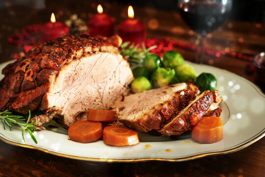 Christmas ham or roast pork with crispy fat crust, served with vegetables on a dark wooden table with candles and bokeh bubbles, selected focus