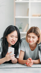 Device leisure. Technology youth. Two friends girls enjoying smartphone gadget internet social media content fun resting in light interior on floor at home.