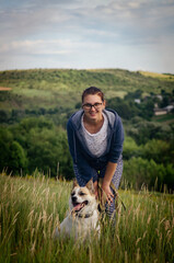 Beautiful girl in glasses walks with a dog in the mountains. The girl stands leaning forward