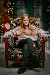 Young teenager girl sit on the chair near decorated Christmas tree. Season greetings