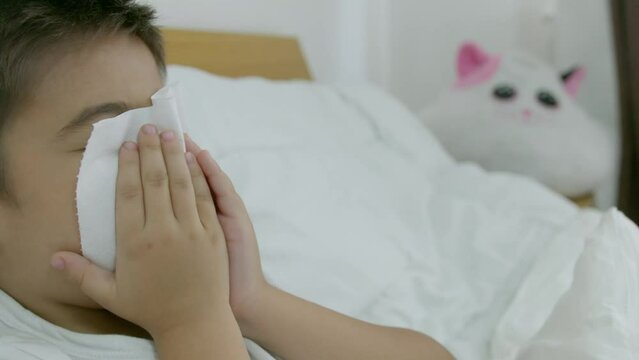 Caucasian boy child in the bed feeling unwell blowing his nose symptom for cold or bronchitis. Healthcare concept. Slow motion. High quality 4k footage