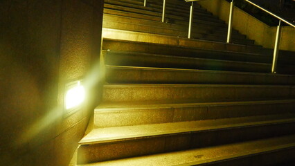Grand plan d'escalier éclairé par des projecteurs de lumière blanche ou jaune, vide, construction urbaine et taillé dans la roche, peu d'éclairage, longue marche, solitude, silence, monté ou descente
