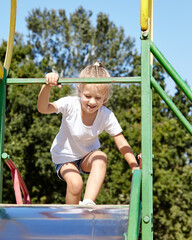 Obraz premium Little girl playing on a slide in a playground in the summer city park. Childhood, leisure and people concept - happy child rest and have a good time