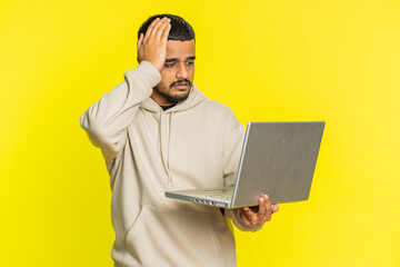 Displeased Indian man use laptop notebook typing browsing working, loses becoming surprised by...