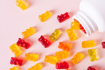 Group of gummy supplements with multivitamins and a bottle for them on a pink top view