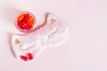 Chewable sleep vitamin supplements and mask on pink background top view