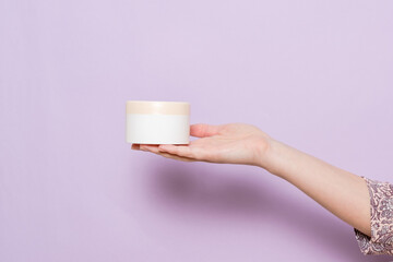 A plastic jar (container) for cream in a woman's hand. Cosmetic product.