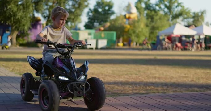 A child driving a toy electric car in a park on a summer day