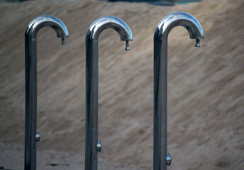 Three nickel-plated shower stands against a sandy beach background - 684337950