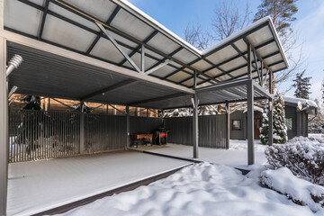 A spacious barbecue gazebo on a snow-covered private territory surrounded by trees.