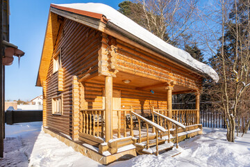 Fototapeta na wymiar A two-story log house, illuminated by the bright winter sun, against a blue sky.