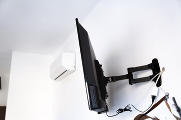 Flat screen TV hanging on a metal mount on the white wall in the room. Black TV bracket, mount bracket for LCD monitor, plasma TV and LED display device. Copy space. Side view