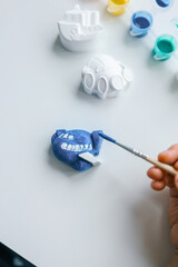Child paints plaster figure with bright colors. Concept of children's creativity. Preschooler does needlework at home