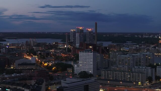 Aerial slide and pan footage of group of high rise buildings and factory with chimneys. Various building in city in evening. Helsinki, Finland