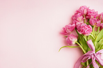 Bouquet of pink peony tulips tied with a pink bow. Spring flowers on the pastel pink background and place for text. Festive concept for Valentines Day or Mother's Day.