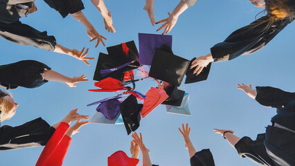 Graduates tossing multicolored hats against a blue sky.